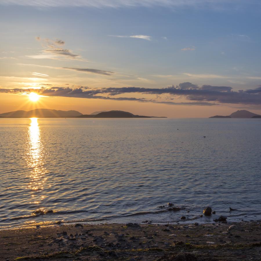 On the beach at the water's edge, a blue and yellow sunset with a streak of clouds above islands in the background.