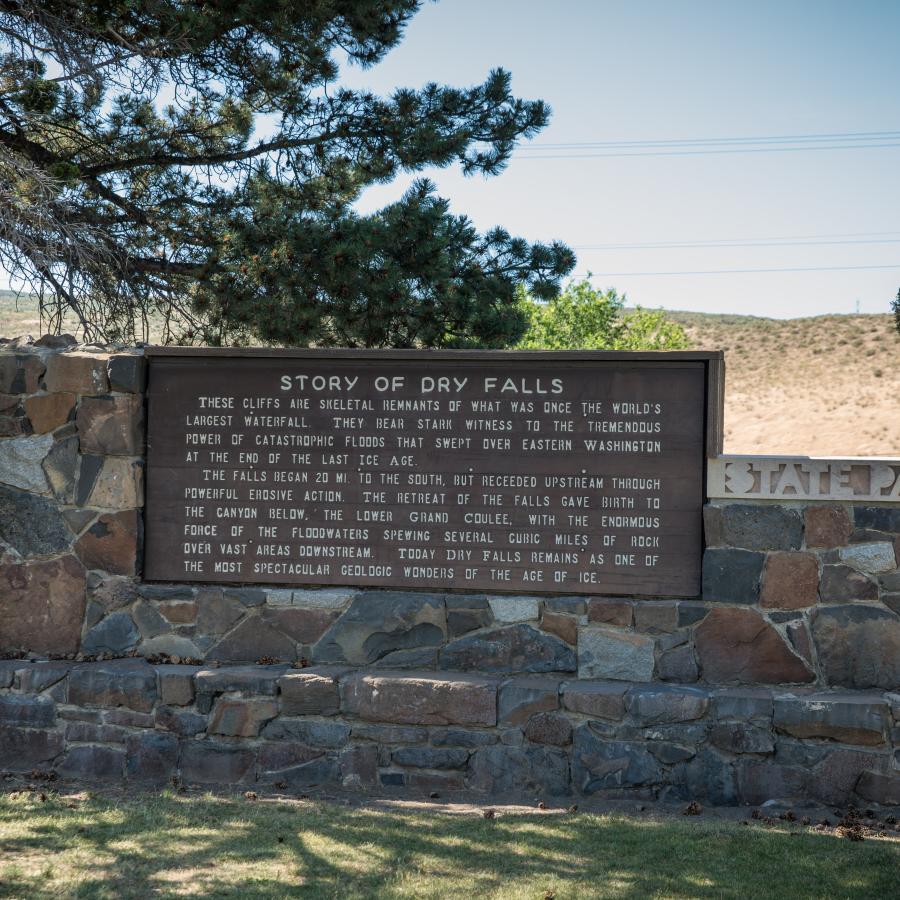 A wood monument depicting the history of Dry Falls sites on a rock foundation.