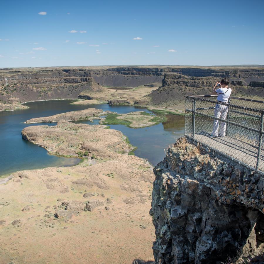 A guest taking a photo of the Dry Falls at the end of the viewing deck.