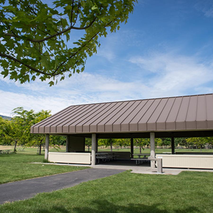 A picnic shelter with a brown roof on a wide green lawn under a bright blue sky.