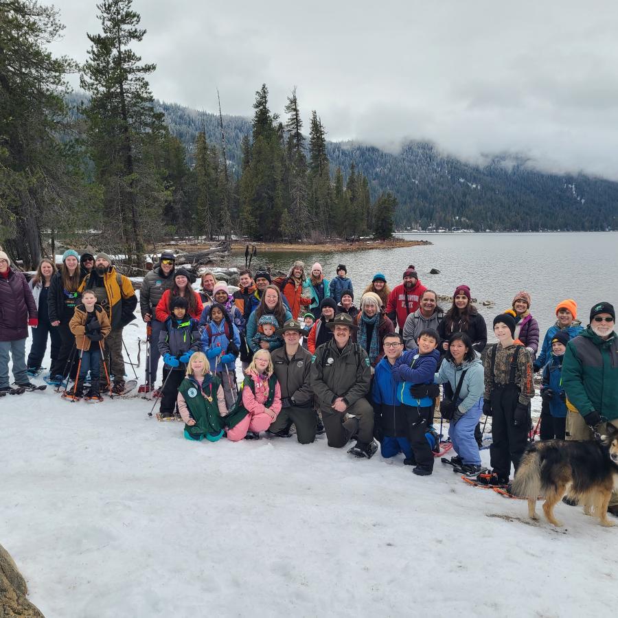 Large group of hikers standing in snow, in front of Lake Wenatchee