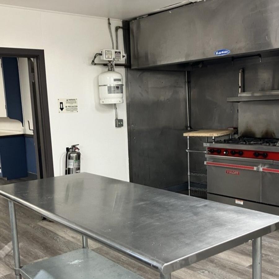 shiny aluminum kitchen prep table with gas stove and range behind it