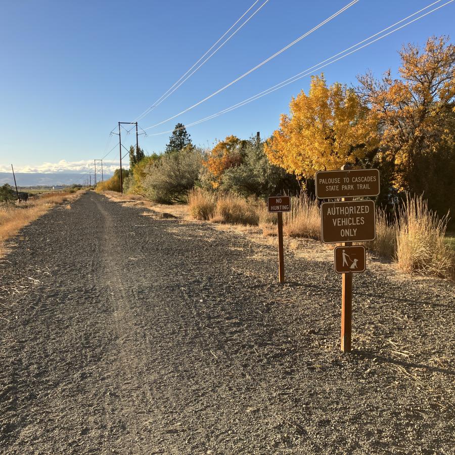 Fall trees line a gravel trail with a sign that says Palouse to Cascades Trail