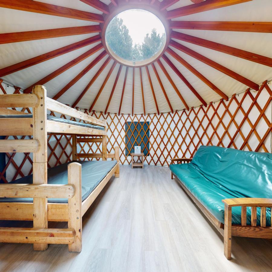 Inside of yurt w/ bunk bed, futon couch and a circle skylight cascading sunlight within the yurt. 