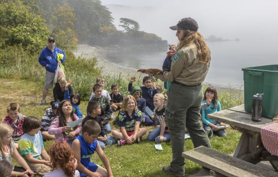 Group of young children sitting on the grass listen to a ranger talk