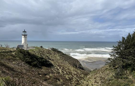Standing on a rocky shore, looking towards the ocean, North Head Lighthouse is white against a stormy grey sky.