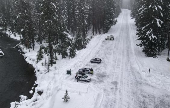 The parking area for the Hells Crossing Sno-Park with a plowed road and a parking area with packed snow and trees. 