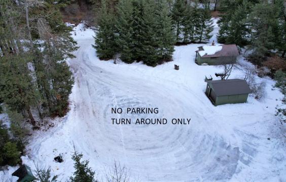 A cul-de-sac covered by compacted thin ice and snow labeled with the words "NO PARKING TURN AROUND ONLY", with two small building structures and surrounded by trees.