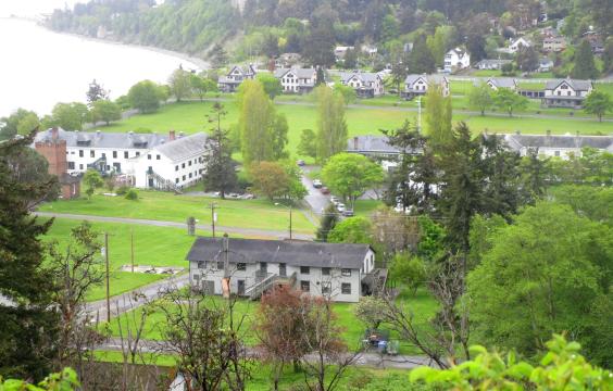 Aerial view of Fort Worden's upper campus. There are green trees and grass and a few white buildings along  the waterfront.