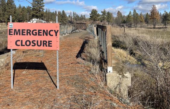 An emergency closure sign in front of a bridge that has been burned in a fire.